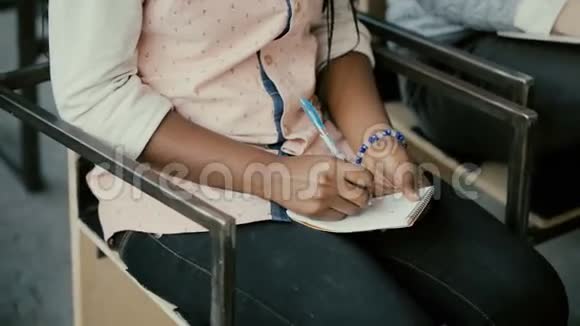 非洲女性手的特写镜头女人坐在椅子上写着笔记本学生女孩在讲课视频的预览图