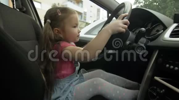 一个小快乐的女孩坐在汽车的车轮后面一辆新车上的小孩的肖像视频的预览图