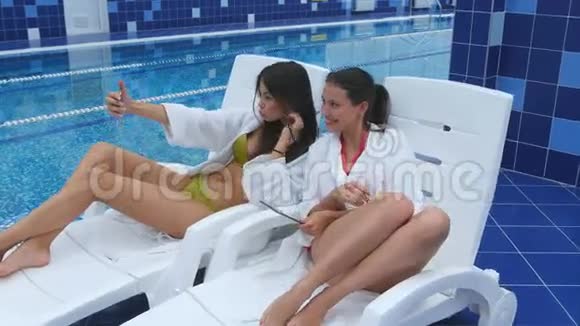 两个美丽的女人坐在游泳池附近的躺椅上自拍视频的预览图