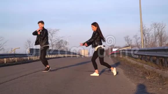一对穿着皮夹克和黑色裤子的舞者在早晨的道路上跳舞动作缓慢视频的预览图