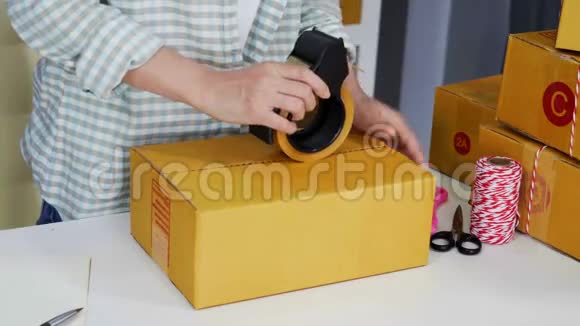 网上女企业家用胶带在家庭办公室包装包裹盒准备产品送货上门视频的预览图