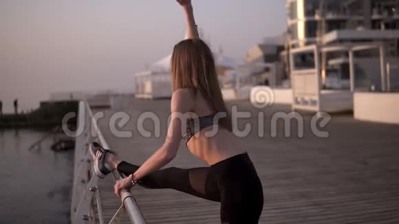 瘦和适合年轻女性穿运动服装伸展腿部肌肉在一个海域穿着黑色紧身裤和灰色胸罩视频的预览图