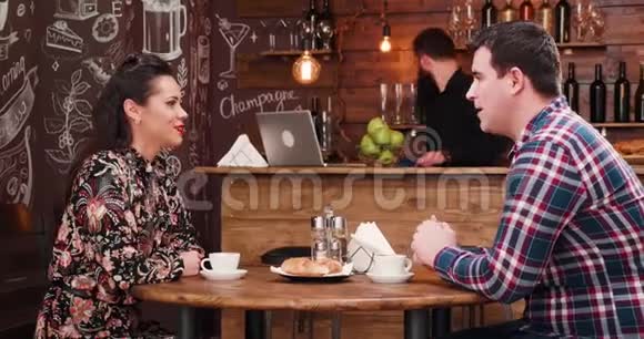 漂亮的夫妇在时尚的咖啡店餐厅酒吧里吃羊角面包和喝咖啡视频的预览图