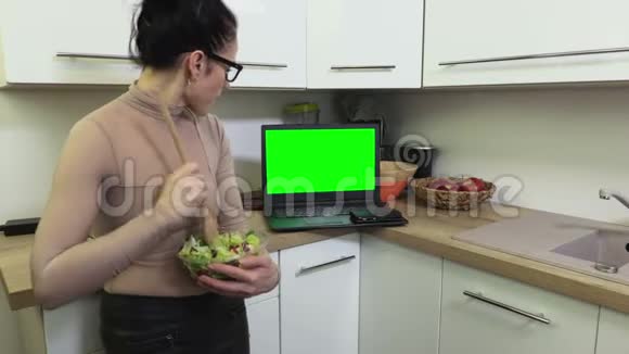 女士品尝沙拉和观看带有绿色屏幕的笔记本电脑视频的预览图