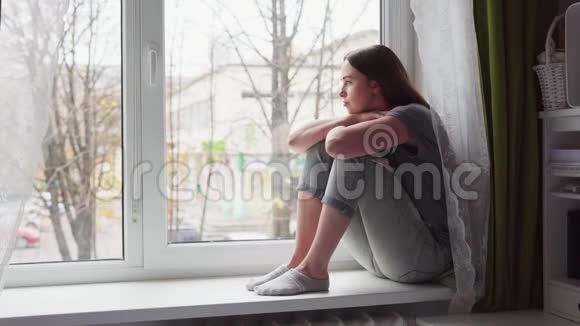 伤心的女人坐在窗台上看着秋天的阴天视频的预览图
