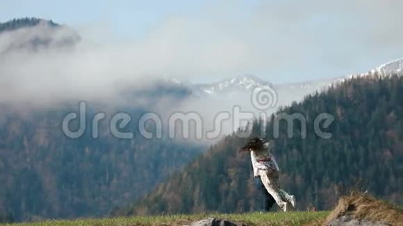 那个男人正在把穿着乡村服装的女孩旋转在草地上在群山环绕的背景下视频的预览图