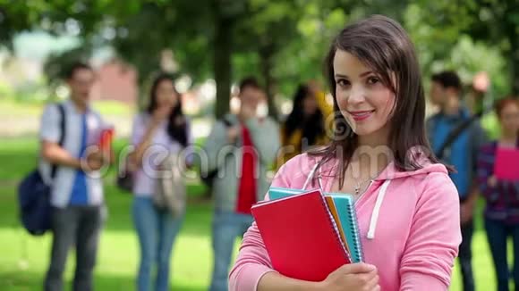 学生在镜头前微笑朋友站在她身后草地上视频的预览图