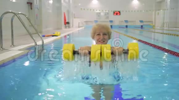 迷人的微笑老年妇女带着哑铃在游泳池视频的预览图