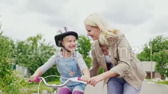 儿童的第一次成功一个女人教她的女儿骑自行车称赞她的成功视频的预览图