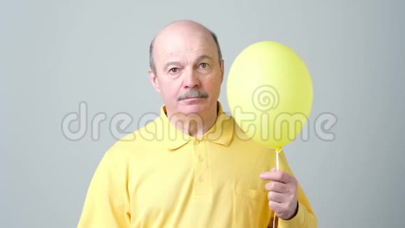 一个穿着黄色衬衫的悲伤老人手里拿着一个小气球视频的预览图