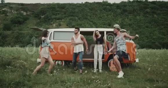 充满魅力的年轻一群朋友在大自然中跳舞在田野的中央在一辆复古的面包车后面4k视频的预览图