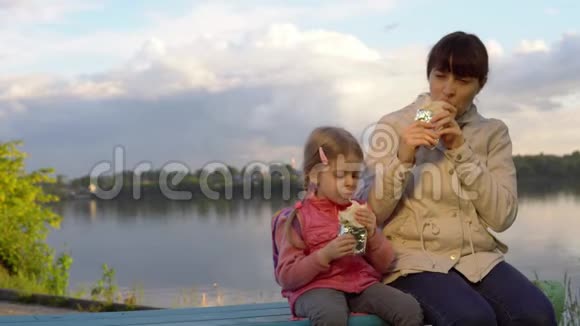 妈妈和女儿一起在池塘旁边的街道上吃甜甜圈视频的预览图