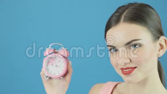 完美CuteBrunette的特写肖像手中有粉红色的时钟在工作室的蓝色背景上有迷人的微笑时间视频的预览图
