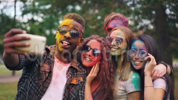 令人兴奋的朋友女孩和男人正在用智能手机用彩色的脸和头发自拍时尚的年轻人是视频的预览图