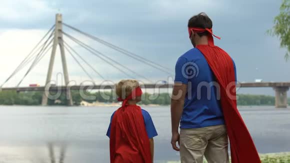 父亲和儿子穿着滑稽的超级英雄服装远远望着支持父母视频的预览图