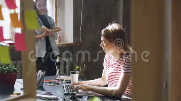 两个漂亮的女孩在现代化的阁楼办公室里一起工作金发女人坐在桌旁用笔记本电脑打字视频的预览图