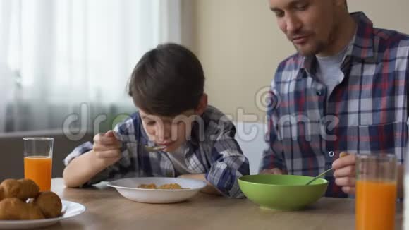 高兴的儿子和父亲在早餐时吃美味的玉米片早晨的传统视频的预览图