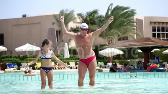 戴着太阳眼镜的男人爸爸和女儿小女孩在游泳池里跳舞一起玩快乐家庭放松视频的预览图