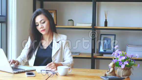 4K镜头忙碌的商务女性用手提电脑工作在书上写作在工作空间里认真思考视频的预览图