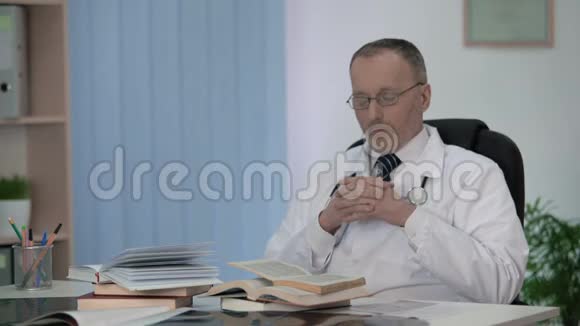 医生坐在书堆前为他的研究工作思考主题视频的预览图