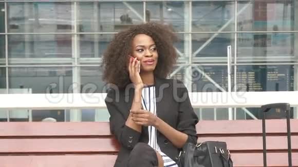 一位迷人的年轻微笑的非裔美国商务女性坐在机场的长凳上谈论着视频的预览图