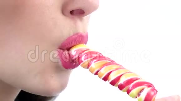 女人舔着白色背景上粉红色发亮的棒棒糖特写视频的预览图