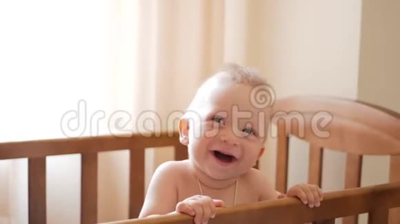 婴儿站在家里的婴儿床上小男孩学着站在婴儿床上视频的预览图