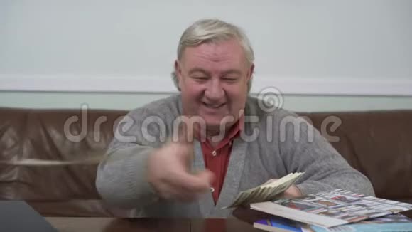 快乐的老人近距离地把坐在木桌旁的美元扔掉了积极向上的富人展示他的财富视频的预览图