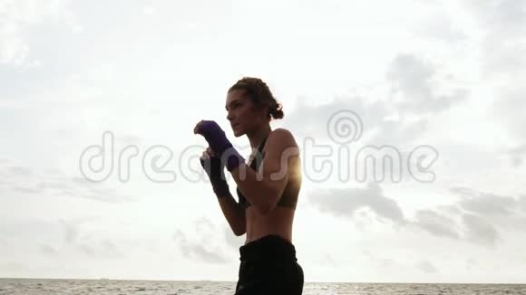 坚强的漂亮女人影子拳击早上美丽的女拳击手在海边训练投掷视频的预览图