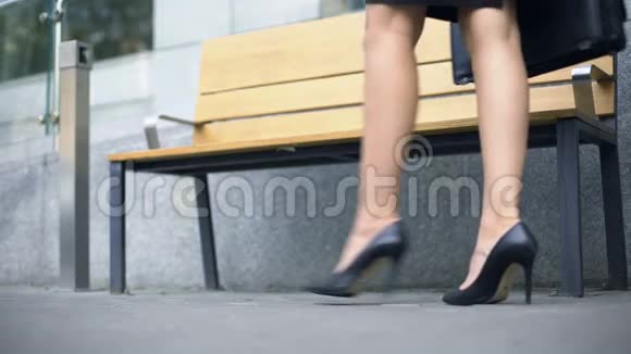 女人坐在长凳上厌倦了穿着不舒服的高跟鞋走路视频的预览图