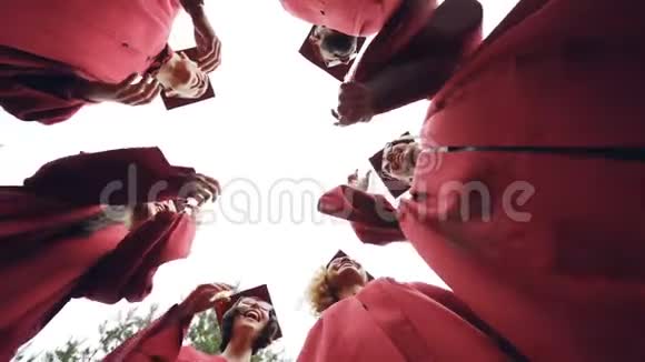 慢动作低角度拍摄的毕业生站成一圈扔灰泥板在天空和笑团结视频的预览图