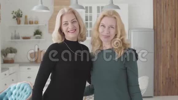 两个微笑成熟的白种人女人站在豪华的厨房里看着镜头富有的资深女性朋友视频的预览图