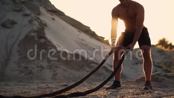 太阳落山时运动的人在沙山周围锻炼把绳子打在地上扬起灰尘视频的预览图
