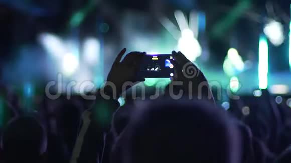 男性手举着智能手机在空中在舞台上拍摄惊人的表演慢镜头视频的预览图
