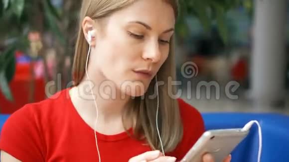 穿着红色T恤的女人坐在咖啡馆里用智能手机听音乐喝着纸杯里的可乐视频的预览图