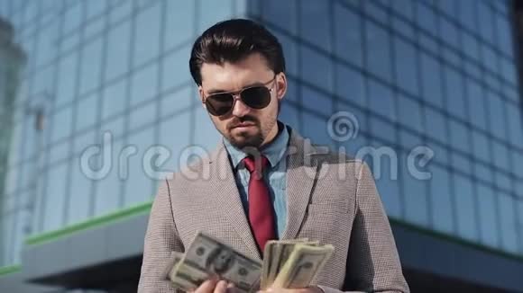 贪婪的富人穿着时髦的西装戴着太阳镜数着钱看着街上的摄像机他是视频的预览图
