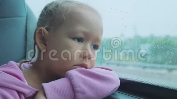 悲伤的孩子在乘公共汽车旅行时望着潮湿的窗户外的肖像视频的预览图