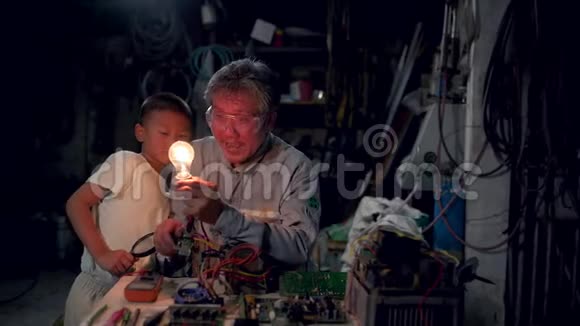 年长的祖父和孙子坐在房子前面的椅子上一起享受灯泡视频的预览图