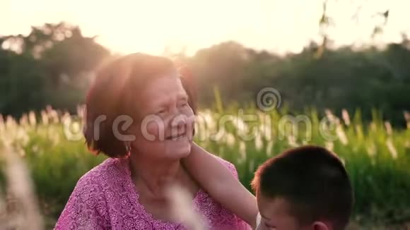 快乐的孙子和奶奶坐在草地上在日落时在公园里玩得很开心视频的预览图