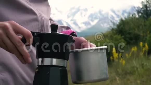 在山里露营一个女孩正在用间歇泉咖啡机准备咖啡一个女人倒在铝制杯子里视频的预览图