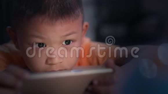 孩子玩手机用手揉眼睛可爱的小男孩晚上在家玩手机游戏视频的预览图