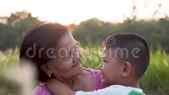 亚洲祖母和孙子坐在草地上在日落时在公园里玩得很开心视频的预览图