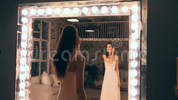 穿着晚礼服的优雅女孩在更衣室灯光下的镜子前摆姿势的肖像布鲁内特视频的预览图