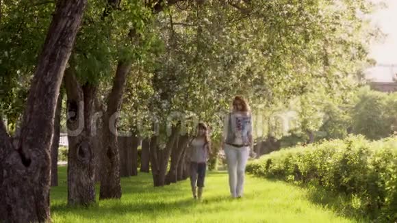 母亲和女儿沿着苹果树的林荫道散步小女孩正牵着妈妈的手儿童视频的预览图