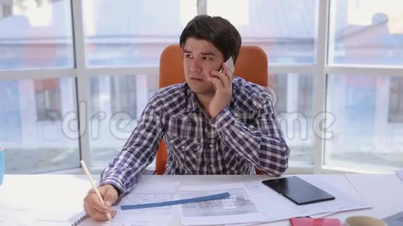 一个自信而有魅力的商人用蓝图工作在一个轻盈现代化的办公室里打电话商务视频的预览图
