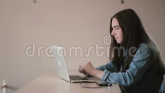 一个十几岁的女孩坐在家里的桌子旁用笔记本电脑上网的画像视频的预览图