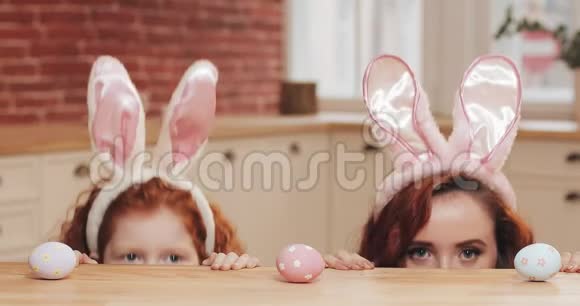 滑稽的妈妈和她的女儿戴着兔子耳朵和复活节彩蛋看镜头的肖像幸福的家庭视频的预览图