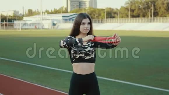 年轻漂亮的女孩在体育场户外做运动漂亮的年轻女孩用弹性带工作健身视频的预览图