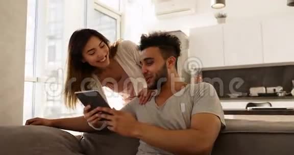 年轻的混血夫妇快乐的西班牙男人坐在教练亚洲女人一起使用平板电脑视频的预览图