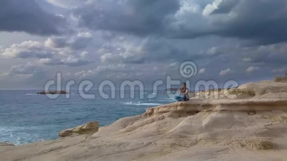 一个女孩坐在海边的岩石上视频的预览图